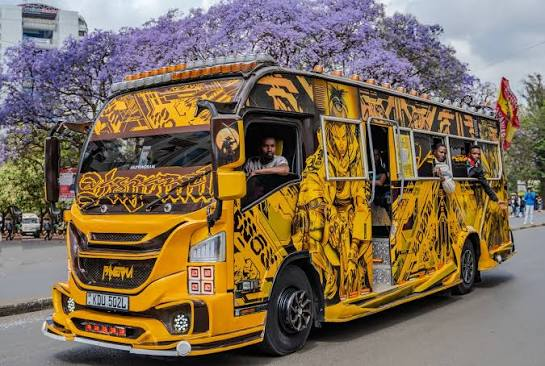 A yellow art-covered Nairobi matatu on the road under jacaranda trees